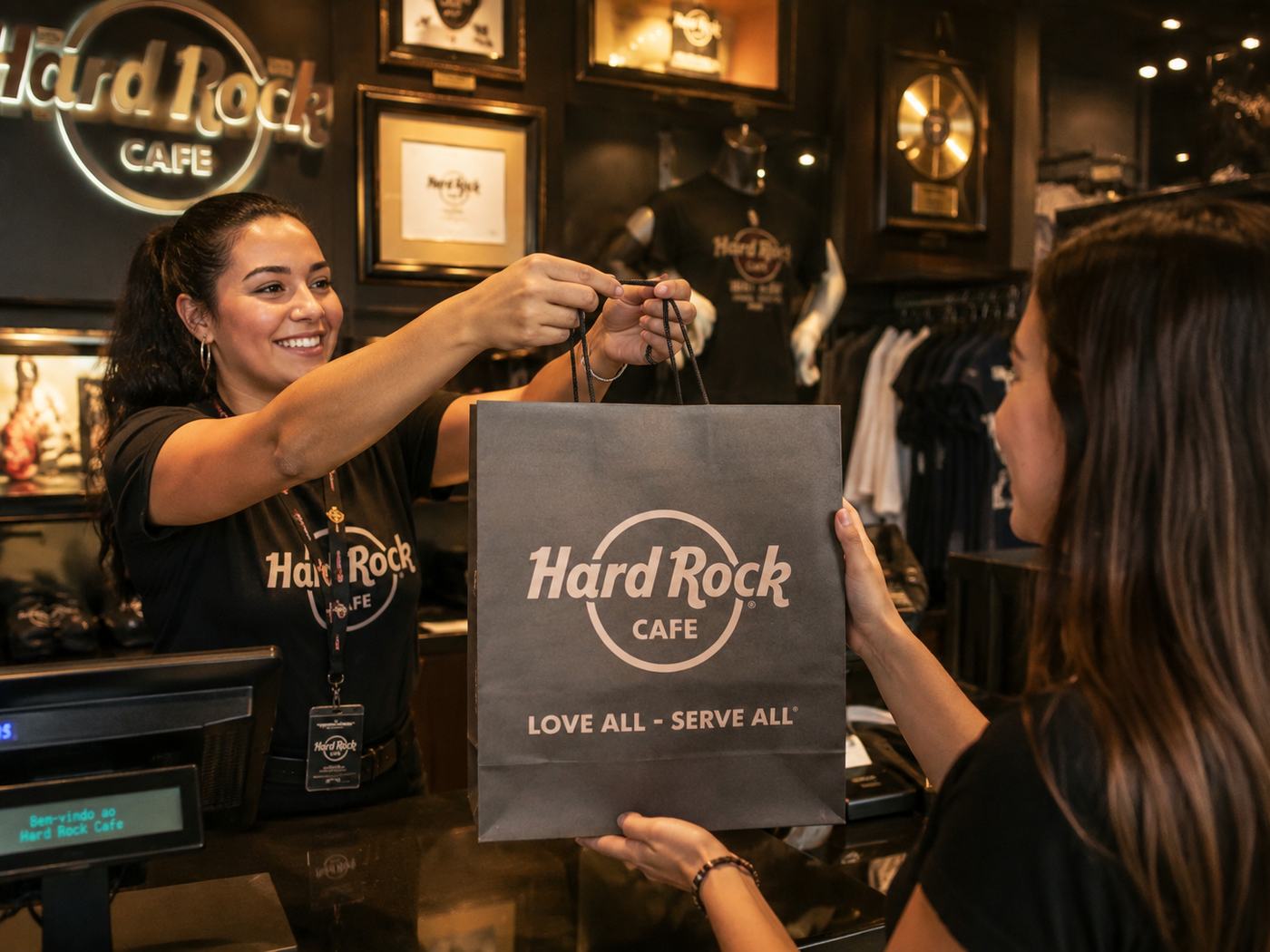 Atendente entregando sacola premium personalizada ao cliente na loja do Hard Rock Cafe